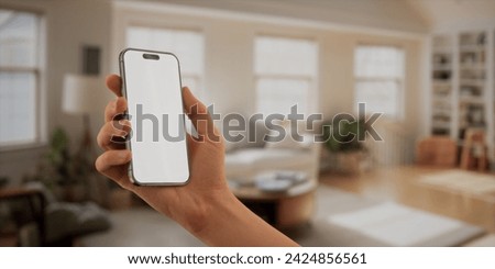 CU Caucasian man using his Apple iPhone 15 Pro phone at home. Daytime shot, furnished house interior in the background. Blank screen, smartphone mockup Royalty-Free Stock Photo #2424856561
