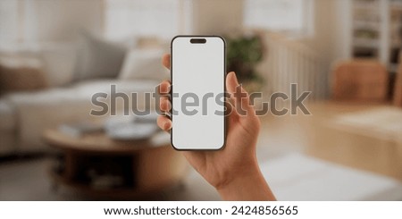 CU Caucasian man using his Apple iPhone 15 Pro phone at home. Daytime shot, furnished house interior in the background. Blank screen, smartphone mockup