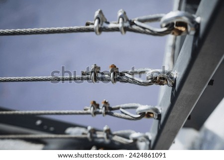 Close-up of intricate gray steel cables and shiny silver fasteners on a modern railing, showcasing an industrial design with strong metal elements and precise alignment in a horizontal pattern. Royalty-Free Stock Photo #2424861091