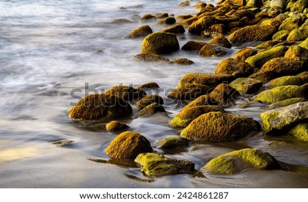 Rocks and pebbles on a tropical beach in the Caribbean sea. Surf water motion with longtime exposure showing flowing streams and rivulets. Natural background with warm contrasting evening sun light. Royalty-Free Stock Photo #2424861287