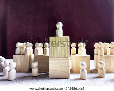 Wooden toy doll on high pedestal and many other figures below. Concept of leadership, which is not available to everyone. Victory and the winner. Talent, Recruitment employee and Successful business Royalty-Free Stock Photo #2424861465