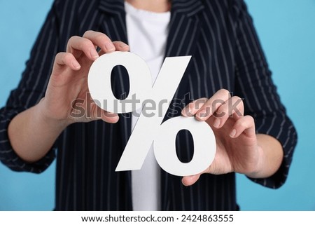 Woman holding percent sign on light blue background, closeup