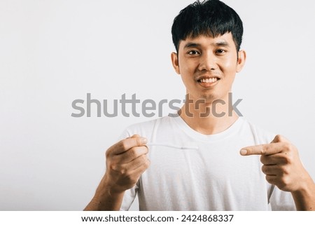 Portrait of a young Asian man, a teen, with a toothbrush, smiling while brushing teeth and pointing to it. Studio shot isolated on white, emphasizing dental health with a positive vibe.
