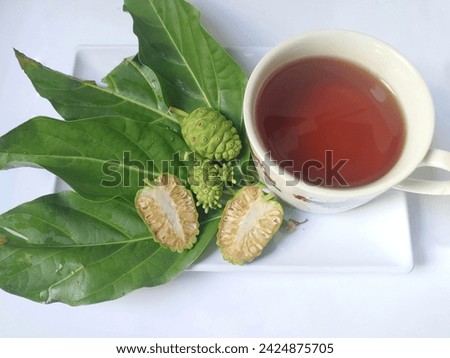 Noni fruit or Morinda citrifolia (Indian mulberry) with green leaves on tree branch. Noni fruit and slice on a white plate isolated on white background.