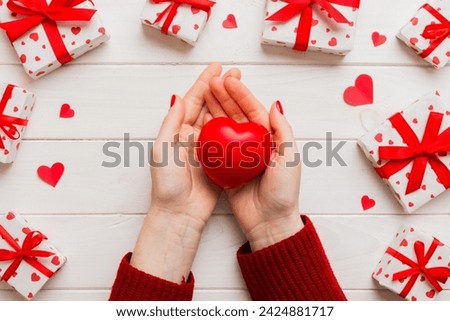 Close up on female hands holding a heart in a colored background for valentine day, birthday, mother's day. Flat lay top view.
