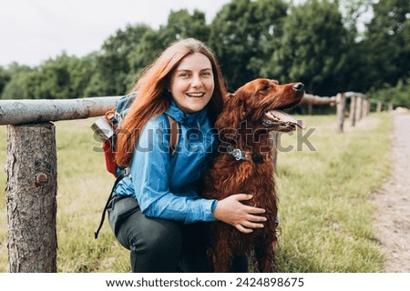 Happy 30s Girl loving and hugging tightly her dog. Travel and hiking with pet. Redhead Woman in active trekking clothes with dog having a halt after hiking, irish setter Royalty-Free Stock Photo #2424898675