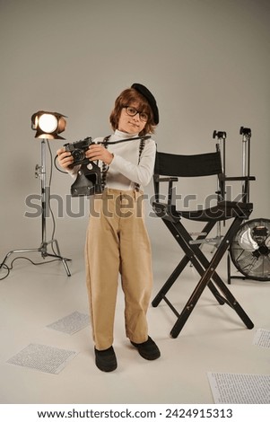 boy in beret and glasses captures the moment on retro camera near director chair, young photographer