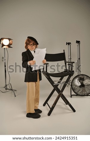 well-dressed boy in glasses and beret holding screenplay on papers, kid as director of filmmaker Royalty-Free Stock Photo #2424915351