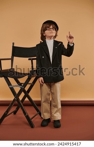 inspired boy stands proudly next to director chair, with a big smile on face showing idea sign