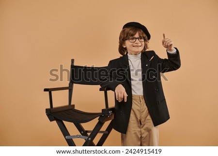 cheerful boy standing near director chair, with a smile on face showing idea sign,  profession