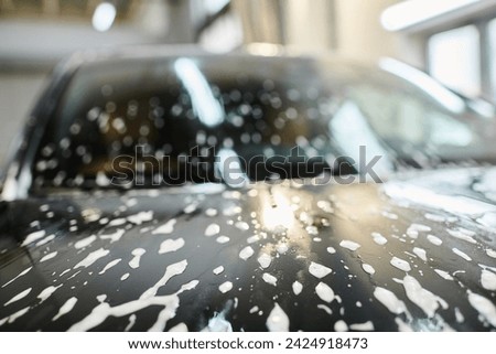 object photo of soapy hood of black modern automobile during car detailing service in garage