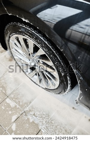object photo of shiny tires of black modern car covered with soap during washing process in garage