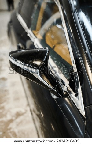 object photo of soapy shiny side view mirror of black modern car during washing process in garage