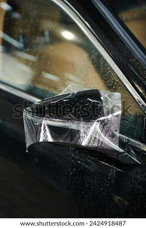 object photo of side view mirror of black modern car with partly applied protective foil on it