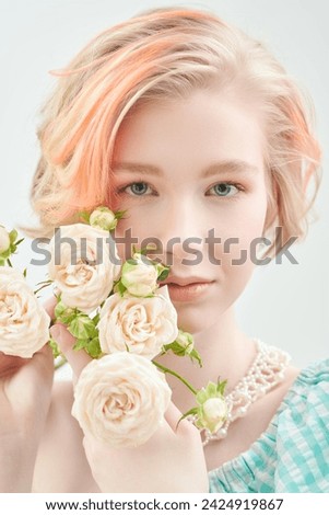 Beauty portrait. A tender blonde girl with a short haircut poses with cream rose flowers on a white studio background. Delicate feminine spring-summer look.