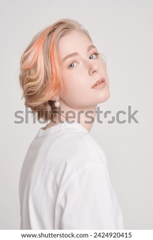 A cute teenage girl with a short haircut and blonde hair with orange streaks poses in a white T-shirt on a white studio background. Adolescence. Beauty, style and fashion.