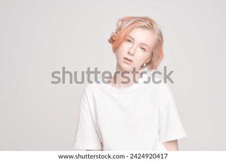 Youth style. A cute teenage girl with a short haircut and blonde hair with orange streaks poses in a white T-shirt on a white studio background. Adolescence. Beauty and Fashion.