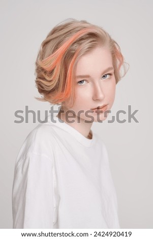 Beauty, style and fashion. A cute teenage girl with a short haircut and blonde hair with orange streaks poses in a white T-shirt on a white studio background. Adolescence. 