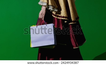 Woman in ancient outfit on the chroma key green screen background. Female in renaissance style dress walking with many shopping gift bags.
