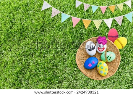 Happy Easter background idea, Colorful Easter egg design in round wooden tray with vintage bunting flag on green grass background Royalty-Free Stock Photo #2424938321