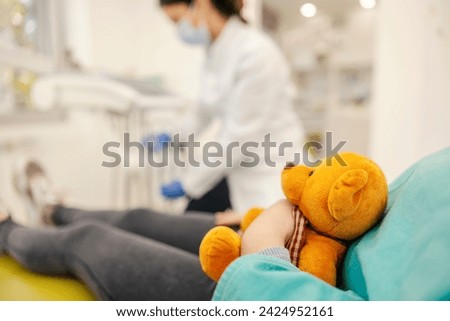 Cropped picture of a girl holding a teddy bear at dentist office.