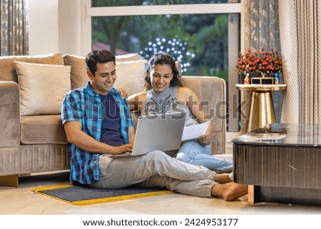 Young wife using laptop while sitting with husband on carpet in living room at home