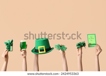 Female hands holding beer and party decor for St. Patrick's Day celebration on beige background