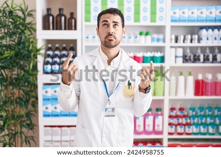 Handsome hispanic man working at pharmacy drugstore pointing up looking sad and upset, indicating direction with fingers, unhappy and depressed.  Royalty-Free Stock Photo #2424958755