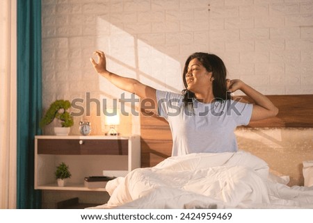 Happy Refreshed woman waking up from bed in the morning by stretching hands - concept of positive emotion, rejuvenation and relaxation Royalty-Free Stock Photo #2424959469