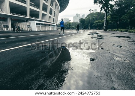Gelora Bung Karno (GBK) Stadium after rain, water reflecting on the running track, with several people jogging in cloudy weather. A sports complex in the capital city of Jakarta, Indonesia.  Royalty-Free Stock Photo #2424972753