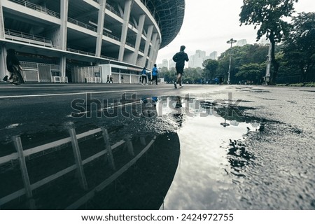 Gelora Bung Karno (GBK) Stadium after rain, water reflecting on the running track, with several people jogging in cloudy weather. A sports complex in the capital city of Jakarta, Indonesia.  Royalty-Free Stock Photo #2424972755