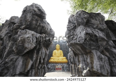 The big golden Buddha statue with waterfall and stone wall in background at Wat Lak Si Rat Samoson, Samut Sakhon, Thailand.
