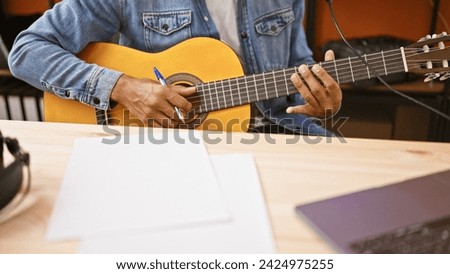 A young man composing music with a guitar in a studio setting, showcasing creativity and artistry. Royalty-Free Stock Photo #2424975255
