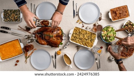 Top down photo of a thanksgiving holiday table spread. Persons arms taking phone picture of turkey.