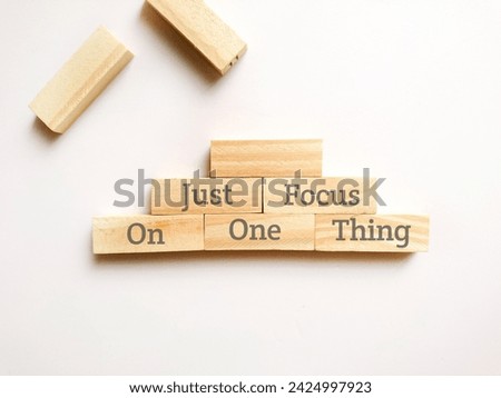 Text written JUST FOCUS ON ONE THING at wooden blocks isolated white background. Motivational quote.