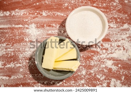Ingredients for baking, butter and sugar in cute plates on a photo background made of scattered flour