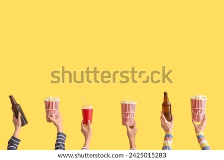 Many hands with buckets of popcorn and beer on yellow background