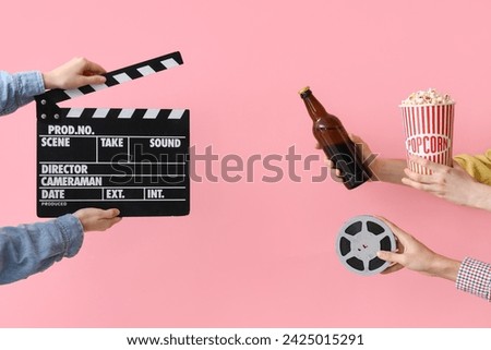 Hands with movie clapper, bucket of popcorn and beer on pink background