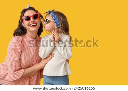 Cute little pin-up girl kissing her mother in sunglasses on yellow background