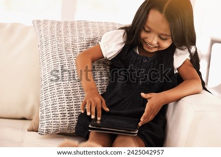 Child, girl and tablet on sofa for entertainment, movie or games in living room at home. Female person or little kid browsing or scrolling on internet with technology for reading or ebook at house
