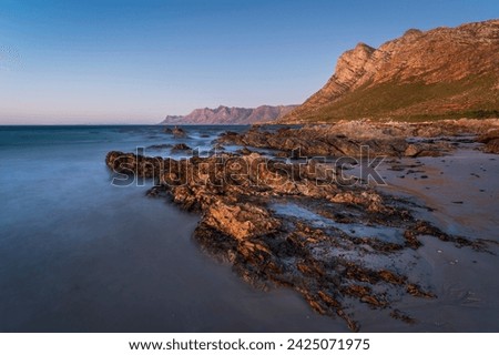 Evening views towards Gordons Bay and the Kogelberg Mountains across False Bay from Rooi-Els beach near Cape Town, Western Cape. South Africa.