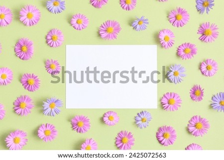 Greeting card template. Pink and purple flower aster on green table background with blank paper sheet. Flat lay, top view, mockup, copy space for text. Aesthetic stylish floral pattern