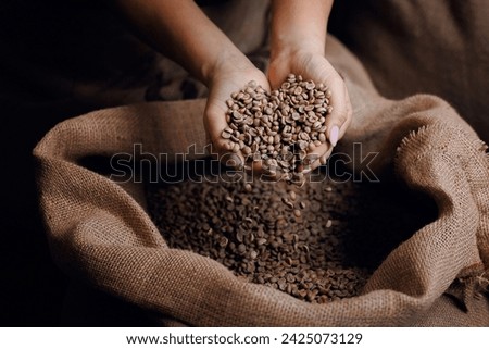 Professional worker hold green coffee beans shaped heart on background jute bag in warehouse. Concept roaster factory, love with espresso. Royalty-Free Stock Photo #2425073129