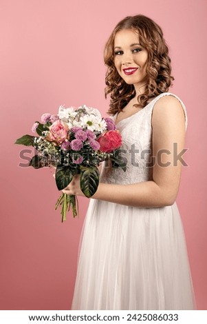 Bride in white wedding dress holds wedding flower in front of the light pink background
