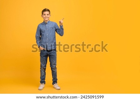 Place For Ad. Happy Male Kid Pointing Aside At Copy Space With Hand, Cheerful Teen Boy Advertising Nice Offer Or Advertisement, Standing Against Yellow Studio Background, Full Length Shot Royalty-Free Stock Photo #2425091599