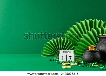 Shamrocks and shenanigans: countdown to St. Paddy's Day. Side view photo of green paper fans, pots, cube calendar, shamrocks, golden coins on green background with space for greetings