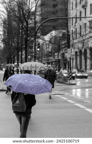 A black and white photo of a woman crossing Georgia Street, carrying a striking purple umbrella. The purple umbrella is the only colored element in the photo.