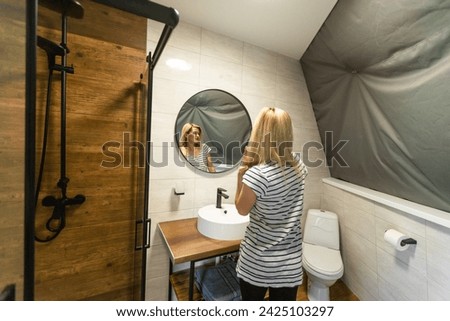 woman touching face skin looking in mirror reflection. Smiling lady pampering, healthy moisturized skin care, aging beauty, skincare treatment cosmetics concept. Royalty-Free Stock Photo #2425103297