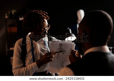 Experienced fashion designer showing couturier sketch drawing of wedding dress she wants him to customize. African american dressmakers working on stylish bespoke sartorial attire