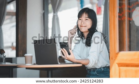 Business analytics concept, A happy Asian woman has a pleasant conversation on her smartphone while using her laptop in a bright and friendly cafe environment.

 Royalty-Free Stock Photo #2425124283